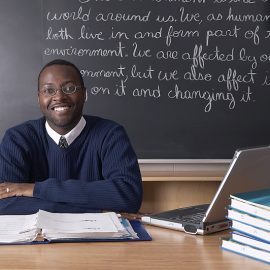 Teacher sitting at desk in front of blackboard