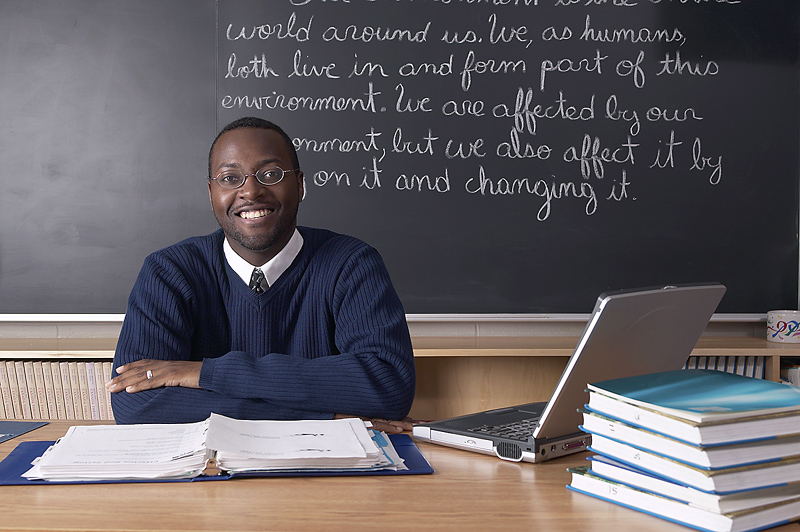 Teacher sitting at desk in front of blackboard