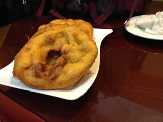 fried dough snacks sitting on a white plate, on top of a wooden table. 