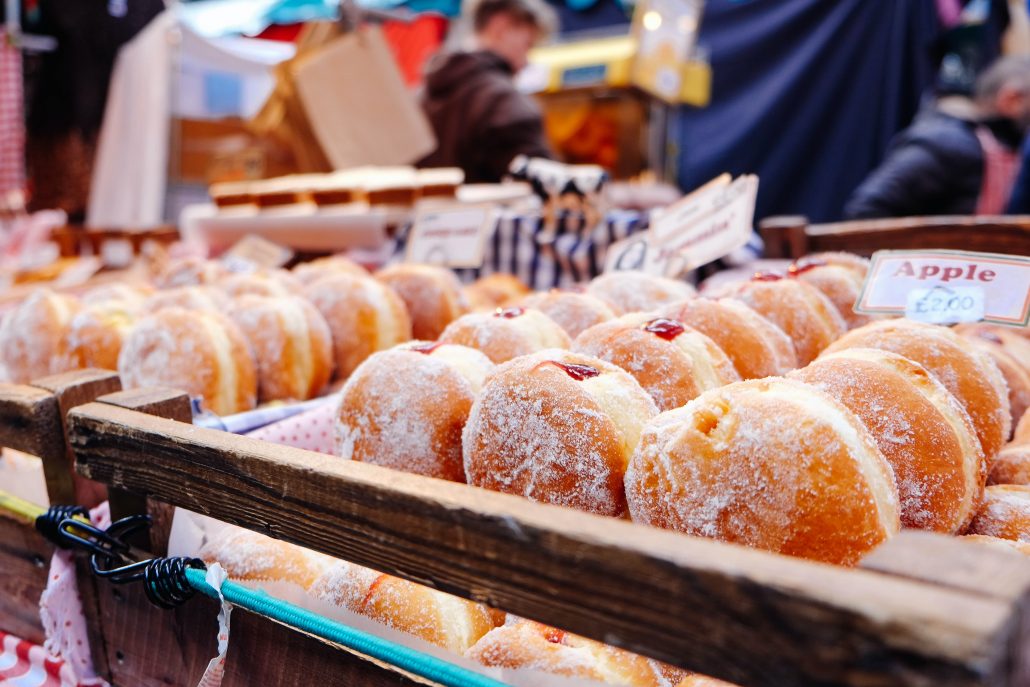 Rows of powdered jelly doughnuts on display at a market. One row is labeled as apple flavored 