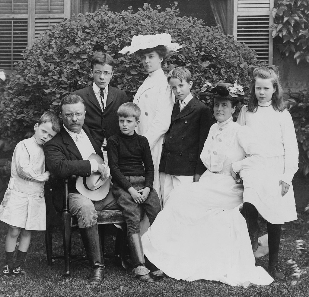 Pres. and Mrs. Theodore Roosevelt seated on lawn, surrounded by their family; 1903. From left to right: Quentin, Theodore Sr., Theodore Jr., Archie, Alice, Kermit, Edith, and Ethel.