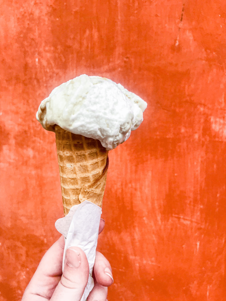 cone with vanilla gelato held by hand in front of orange wall 