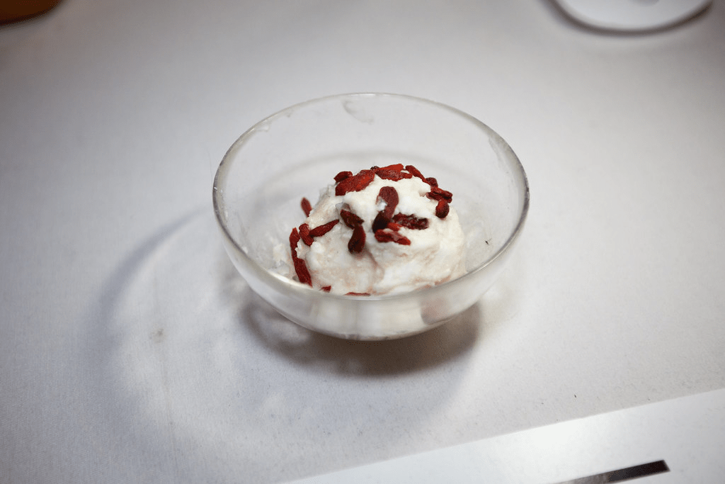 glass bowl of ice cream with berry topping on table 